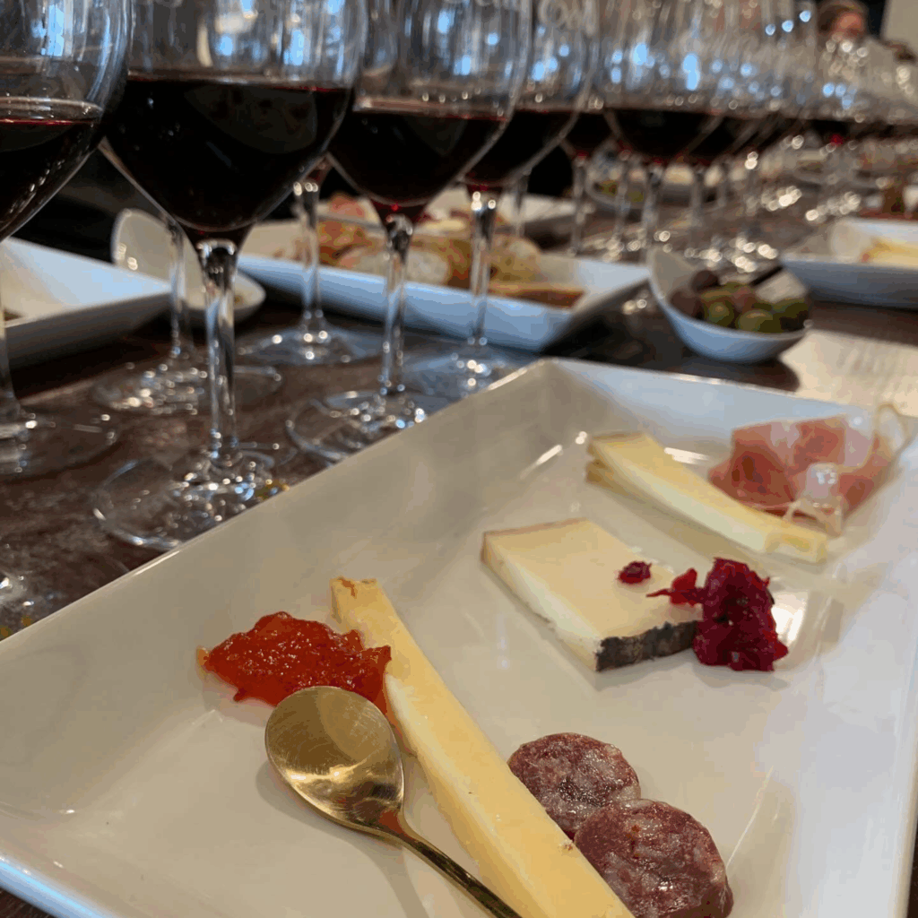 Plate of various cheeses with glasses of Cellar 13 wine behind. From a wine and cheese pairing event.